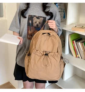 Detail view of khaki pleated drawstring backpack featuring large front pocket and black zipper