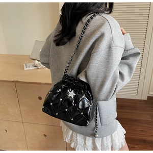 Détail du sac seau matelassé noir avec breloque étoile porté par un mannequin