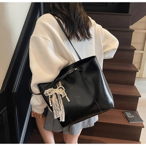 Detail of black glossy PU leather tote bag featuring a pearl lace bow charm on model