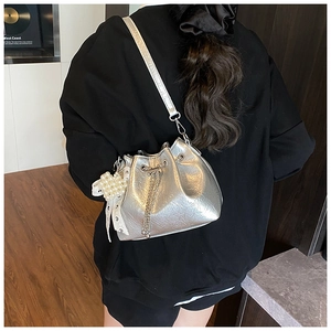 Detail of silver metallic bucket bag with drawstring chain and pearl lace charm accessory