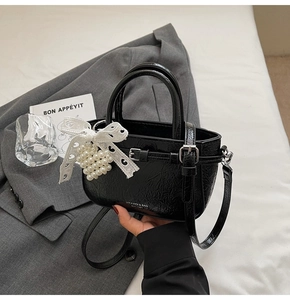 Detail of black embossed leather crossbody bag with lace bow and pearl charm ornament