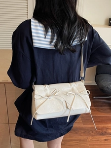 Sac à bandoulière blanc à nœuds en cuir brillant texturé porté par un mannequin