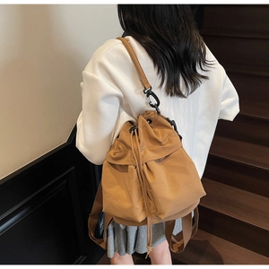 Detailed view of camel drawstring bucket backpack on model in a minimalist indoor setting
