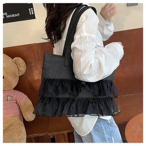 Detail view of black denim tote bag featuring tulle ruffle trim in a cafe lifestyle setting