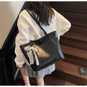 Detail of black PU leather tote bag with lace pearl bow charm on a shoulder