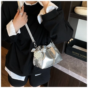 Detail of silver pleated bucket bag featuring pearl heart charm and lace bow accents