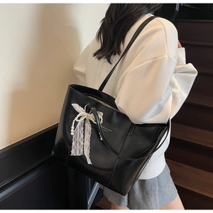 Detail of black PU leather tote bag with white lace bow and pearl pendant on a model
