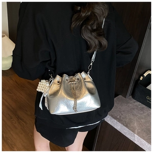 Detail of silver pleated bucket bag with pearl charm and metal chain strap on model