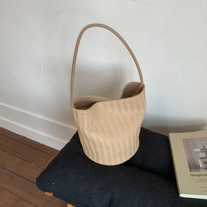 Detailed herringbone texture of beige woven bucket bag on soft grey fabric surface