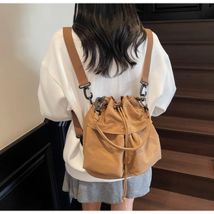 Detail of the camel drawstring bucket bag showing wide fabric straps and matte metal hooks