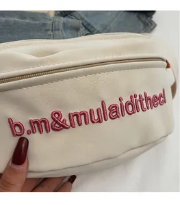 Détail d'un sac banane beige avec logo brodé rose et fermeture éclair sur denim