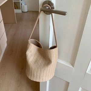 Detail shot of the V-shape woven texture and sturdy round base of a beige bucket bag