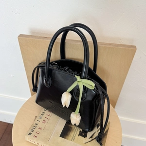 Detail of black glossy bucket bag with Tonton logo and white tulip flower pendant accessory