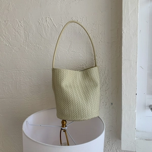 Detail of light green woven bucket bag featuring premium herringbone pattern and shoulder strap