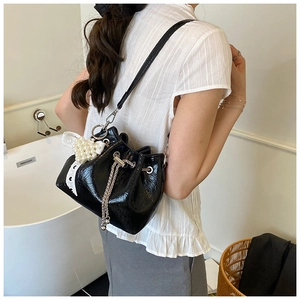 Detail of black patent leather bucket bag with lace bow and pearl charm ornament