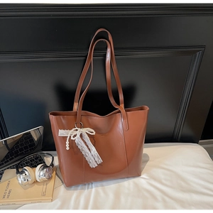 Detail of caramel leather tote bag featuring a vintage lace and pearl bow charm accessory