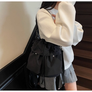 Model wearing a black nylon bucket bag with drawstring closure and silver metallic studs