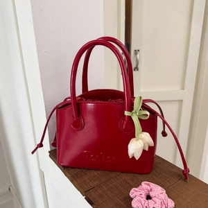 Detail of red glossy handbag with Tonton embossed logo and white tulip floral charm