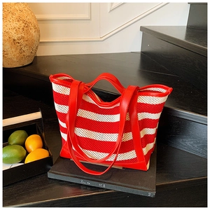 Detail of red and white striped knit tote bag with leather straps on wooden background