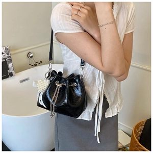 Detail of black glossy drawstring bucket bag with pearl and lace bow charms