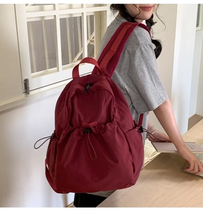 Detailed back view of a burgundy drawstring backpack worn by a model in a casual setting