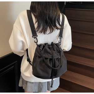 Rear view of black nylon drawstring bucket bag worn by model on stairs