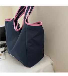 Große marineblaue Segeltuchtasche mit rosa Besatz auf Schreibtisch mit Laptop-Detail