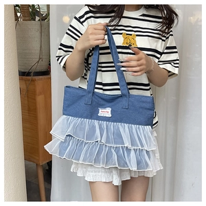 Detail of denim tote bag featuring white layered lace ruffles and Fashion Bag text label