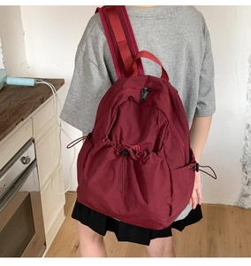 Macro detail of deep burgundy drawstring backpack showing pleated pocket and durable fabric