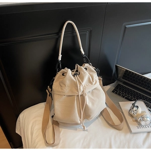 Detail of canvas bucket bag with drawstring closure, beige strap and metal hardware