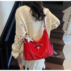 Detail of red glossy hobo bag with bow decoration and silver charms on model