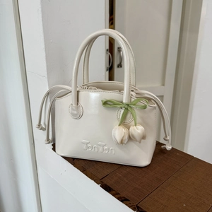 Detail of cream white tote bag featuring embossed logo and silk tulip floral charms