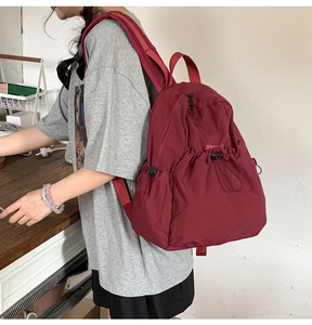 Side view of a burgundy nylon drawstring backpack with adjustable straps on a model