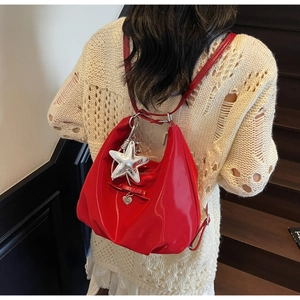 Red glossy leather dumpling bag with star pendant and heart charm on a beige sweater