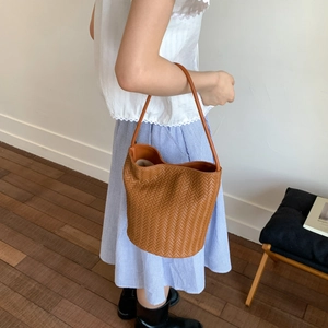 Brown woven bucket bag with thick leather handle shown in a minimalist lifestyle setting