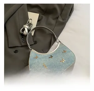 Dettaglio borsa in denim blu con farfalle argentate e tracolla in pelle lucida