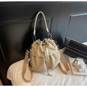 Detail of khaki drawstring bucket bag with black metal hardware on a cozy bed