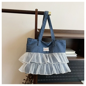 Detail of denim handbag with white tulle ruffle trim and fashion label on dark wood hanger