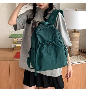 Dark green nylon drawstring backpack worn by model in a cozy indoor home setting