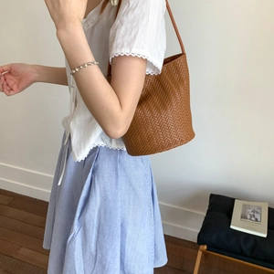 Close-up of brown woven bucket bag with herringbone texture and slim leather shoulder strap