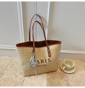 Detail view of large straw tote bag with brown leather handles and star charm