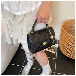 Detail shot of black quilted bag with golden turn-lock and ball charm held by hand