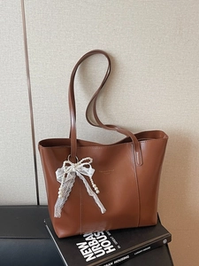 Vintage brown leather tote bag with lace bow and pearl charm on a fashion book background