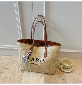 Detail of woven straw tote bag featuring Paris Milano print and silver star tassel charm