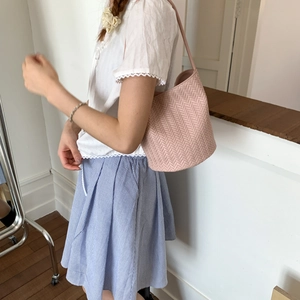 Close-up of pink woven leather bucket bag with V-shaped texture on a shoulder strap