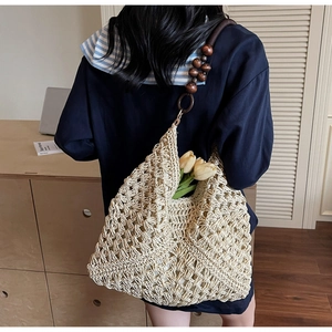 Detail of woven tote bag featuring dark brown strap with large red wooden beads decoration