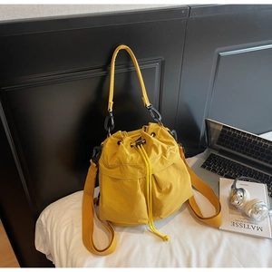 Detail of yellow nylon drawstring bucket bag with adjustable straps on white bedding