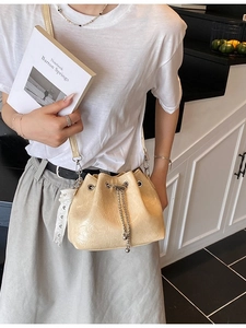Chic beige drawstring bucket bag with shiny pleated leather and chain detail on model