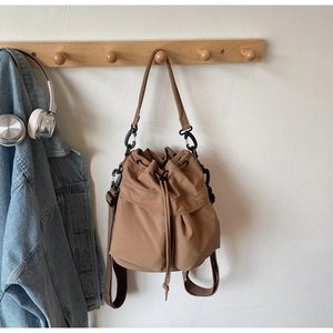 Brown nylon bucket bag with drawstring and detachable straps shown on a wooden hook