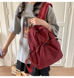 Detail of burgundy nylon drawstring backpack showing waterproof fabric and wide shoulder strap
